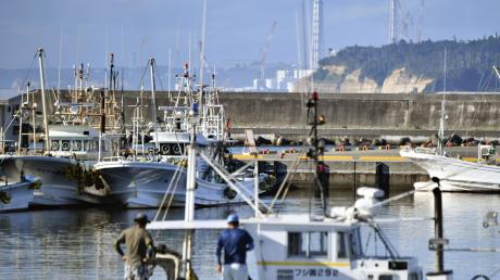 Fischerboote im Hafen von Namie vor dem Hintergrund des havarierten Kernkraftwerks Fukushima Daiichi.