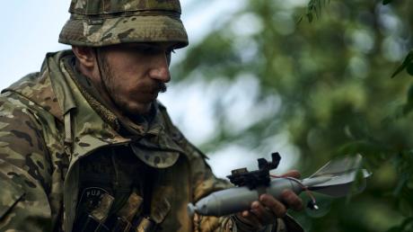 Ein ukrainischer Soldat lädt eine Bombe auf eine Drohne.