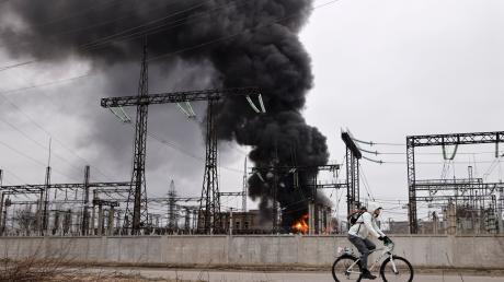 Nach einem russischen Angriff fährt ein Mann mit seinem Rad an einem brennenden Elektrizitätswerk in Charkiw vorbei.