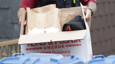 Ein Polizist trägt nach einer Wohnungsdurchsuchung einen Karton mit sichergestellten Gegenständen.