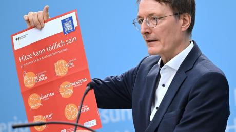 Bundesgesundheitsminister Karl Lauterbach (SPD) hält ein Plakat zum Thema Hitzeschutz hoch.
