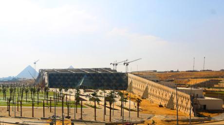Das Große Ägyptische Museum wird ein kolossales Bauwerk. Hinter ihm sieht man die Pyramiden von Giseh auf einem Plateau.