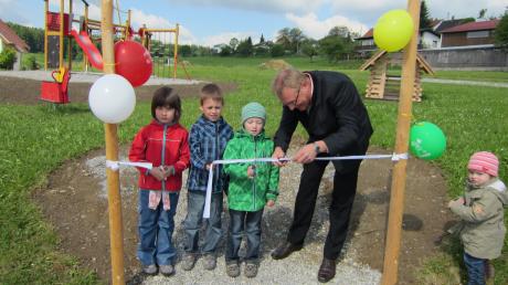 Bürgermeister Robert Wippel durchtrennt zusammen mit den Kindern das Trassenband und eröffnet damit den neuen Spielplatz.
