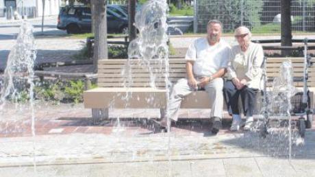 Bürgermeister Klaußner genießt gemeinsam mit einer Bürgerin am neuen Brunnen ein paar Sonnenstrahlen.