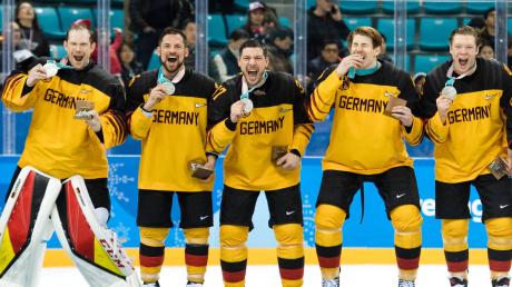 Da ist das Ding! Patrick Reimer (Mitte) präsentiert die Silbermedaille, die er mit der deutschen Eishockey-Nationalmannschaft bei den Olympischen Winterspielen in Südkorea gestern gewonnen hat.