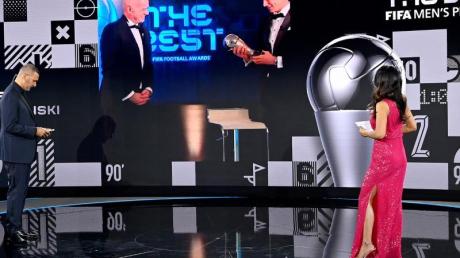 Dem FCB-Stürmer Robert Lewandowski (r. auf Bildschirm) wird 2020 die Weltfußballer-Trophäe überreicht.