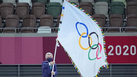 IOC-Präsident Thomas Bach hält die Fahne olympische Fahne hoch.