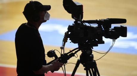 Ein Kameramann steht mit Mundschutz am Rand eines Basketballfeldes.